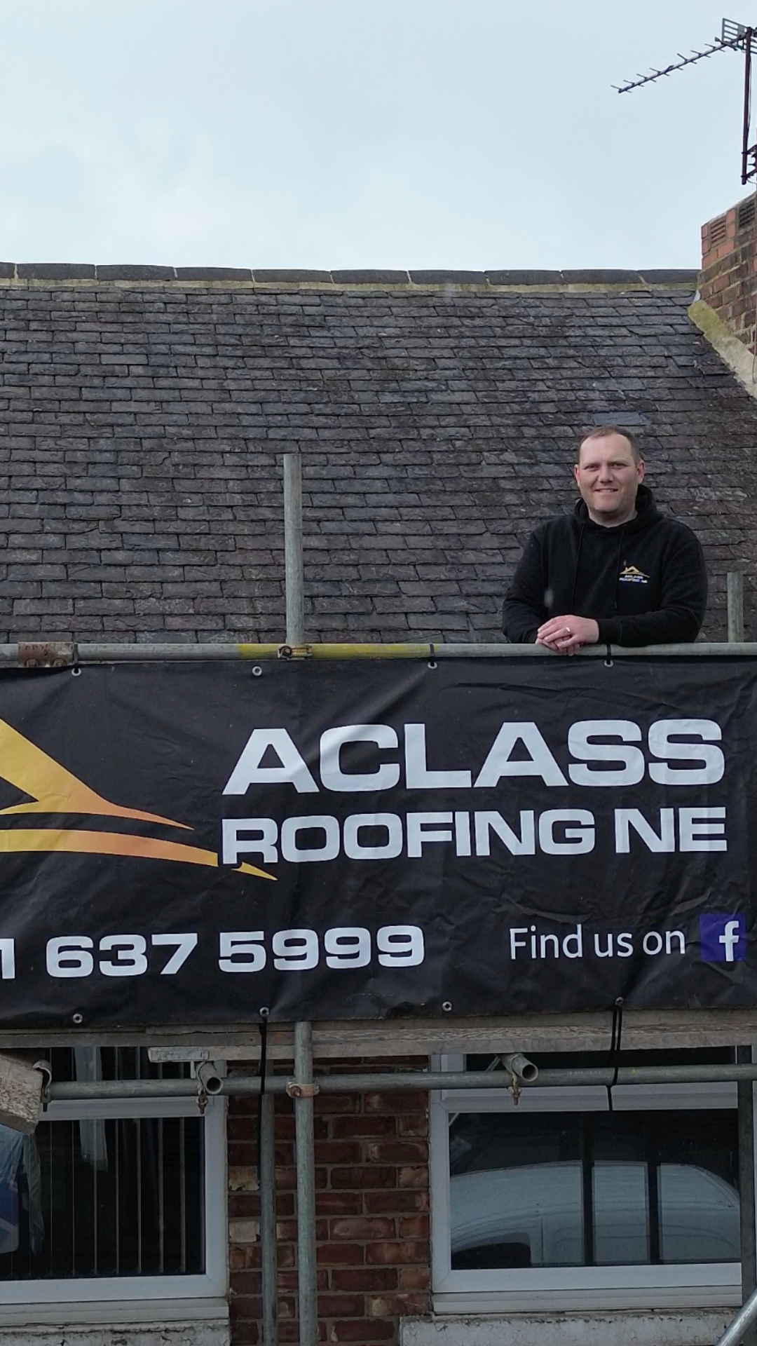 A Class Roofing NE owner standing on scaffolding beside a branded banner during a roof replacement in the North East